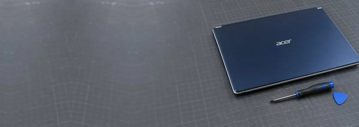 A closed dark-blue Acer laptop with silver trim on a slate-grey workbench beside a screwdriver and an opening pick