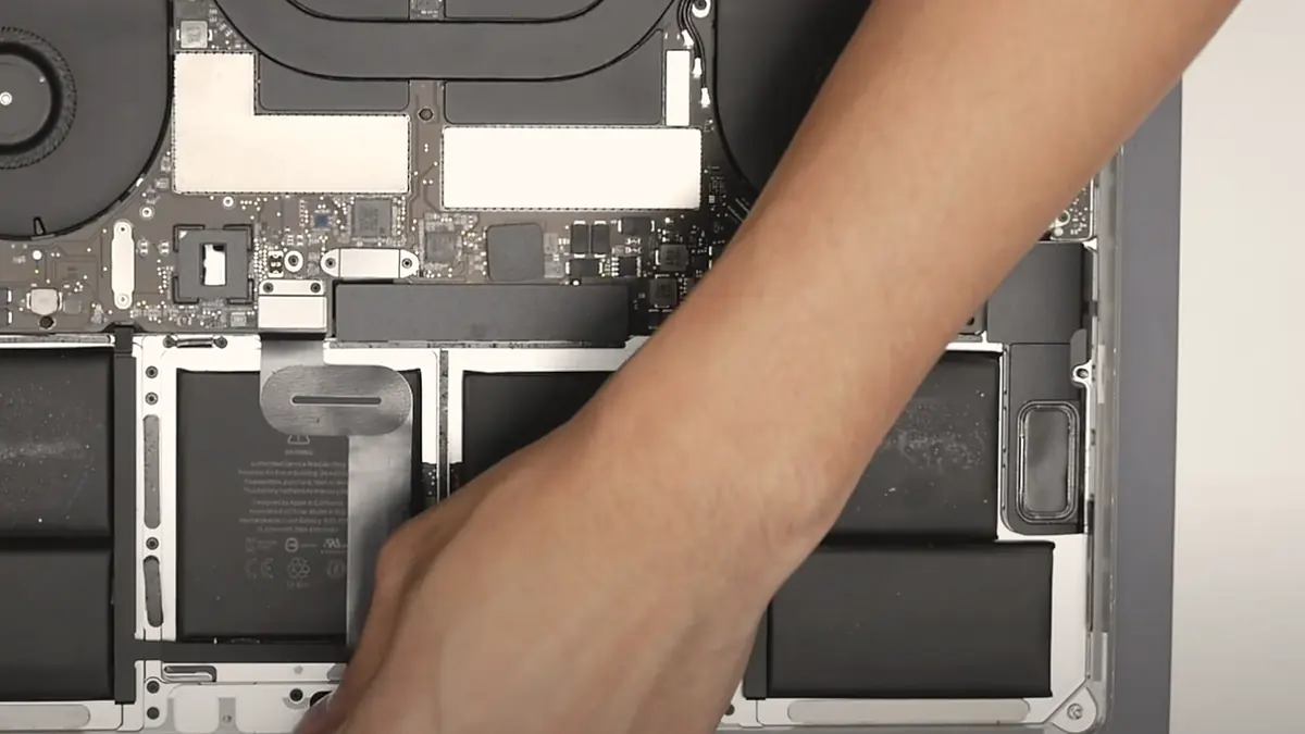 Inside an opened MacBook, with a technician's hand at the battery pull tab