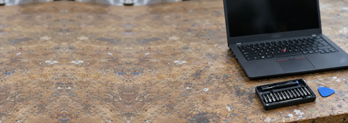 An open dark-grey laptop with its screen switched off on a repair bench beside a screwdriver set and an opening pick