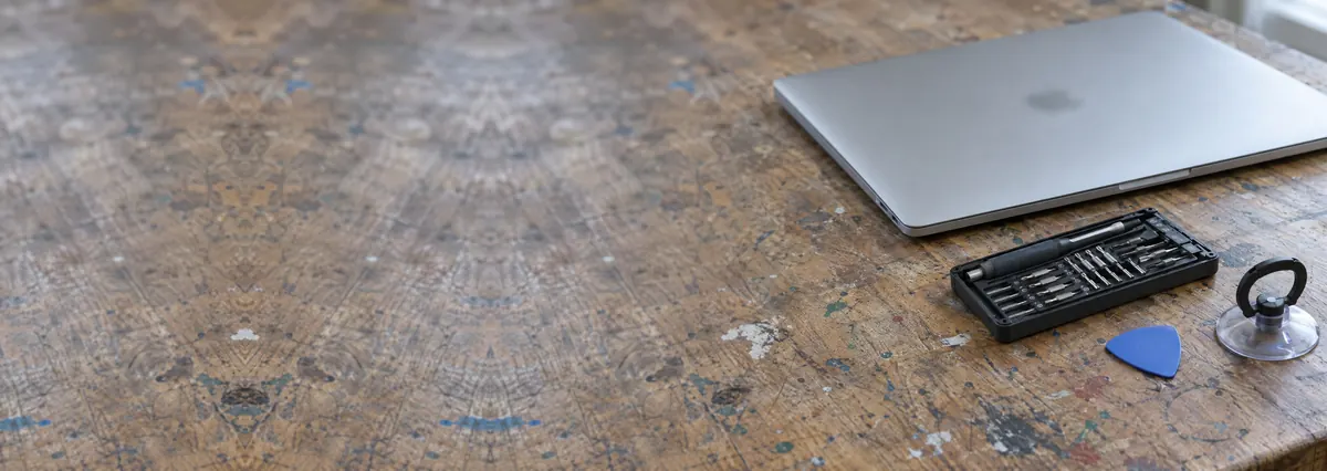 A closed silver laptop in an aluminium case on a repair bench beside a screwdriver set, an opening pick and a suction handle