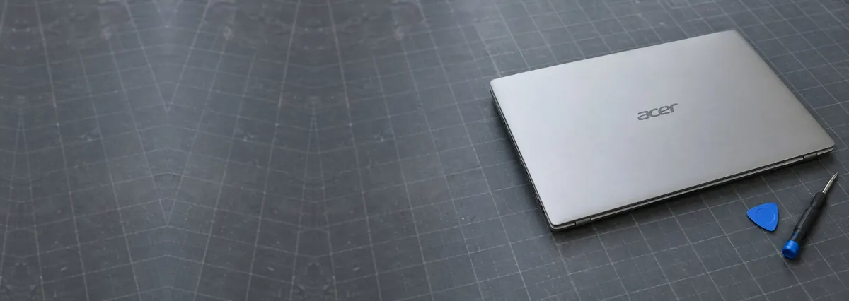 A closed silver Acer laptop beside an opening pick and a screwdriver on a slate-grey workbench