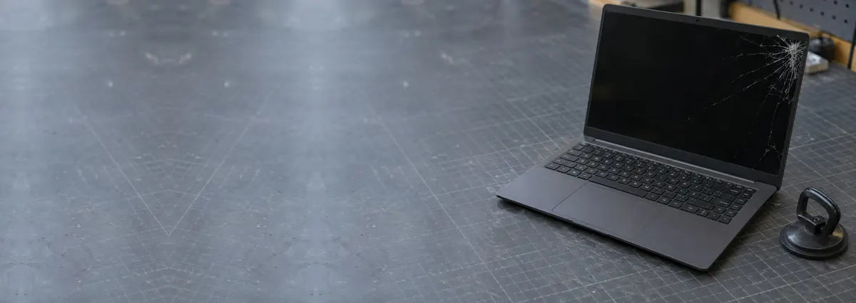An open laptop with a cracked screen beside a suction handle on a slate-grey workbench