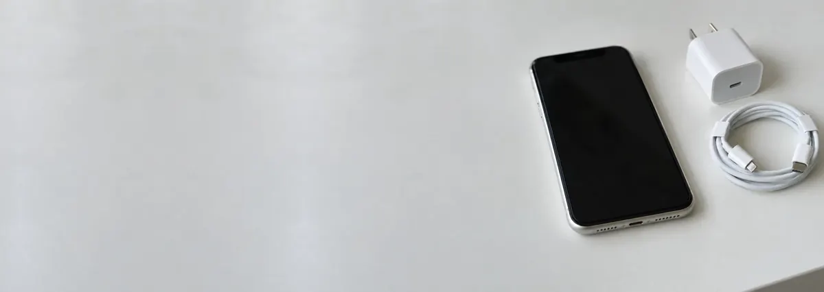 An Apple iPhone beside a charging brick and a cable on a white bench