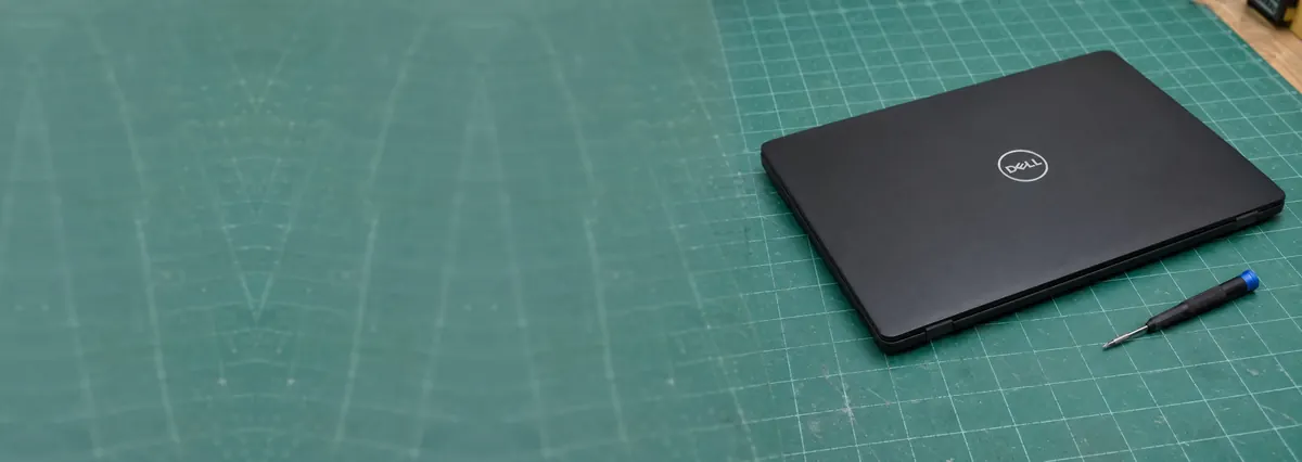 A closed black Dell laptop beside a precision screwdriver on a green cutting mat