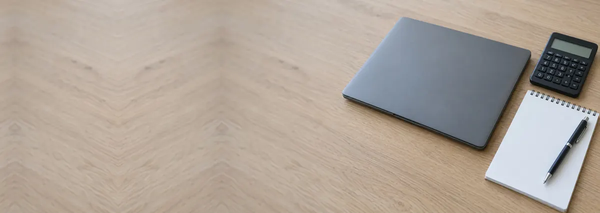 A closed grey laptop beside a small calculator and a notepad on an oak desk top