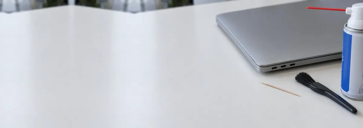 A closed Apple MacBook seen from its side showing its USB-C ports beside a brush, a toothpick and compressed air on a white bench