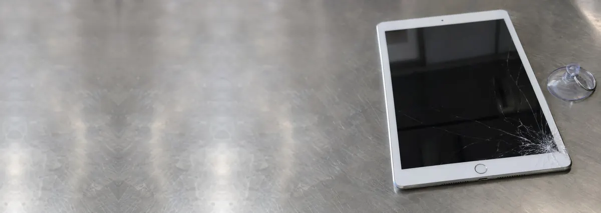 An Apple iPad with a cracked screen beside a suction cup on a steel workbench