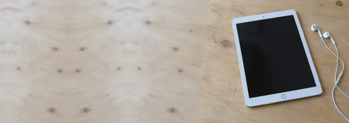 An Apple iPad beside wired earbuds on a plywood bench