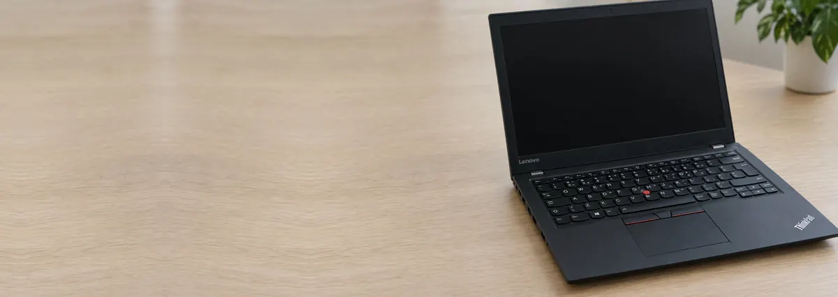 An open black Lenovo ThinkPad with its screen off on an oak desk top