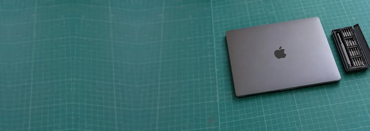 A closed space-grey Apple MacBook Pro beside a precision screwdriver set on a green cutting mat