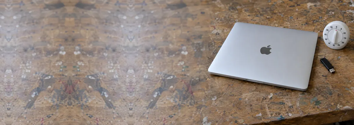 A closed Apple MacBook beside a flash drive and a small kitchen timer on a wooden bench