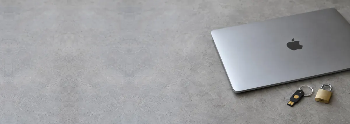 A closed Apple MacBook beside a security key and a padlock on a concrete-effect workbench