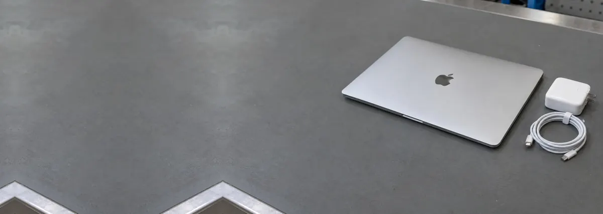 A closed Apple MacBook beside a white charger and cable on a grey anti-static mat
