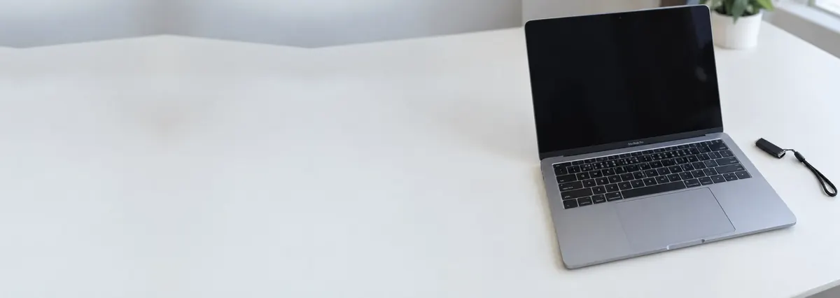 An open Apple MacBook with its screen off beside a flash drive on a lanyard on a white bench