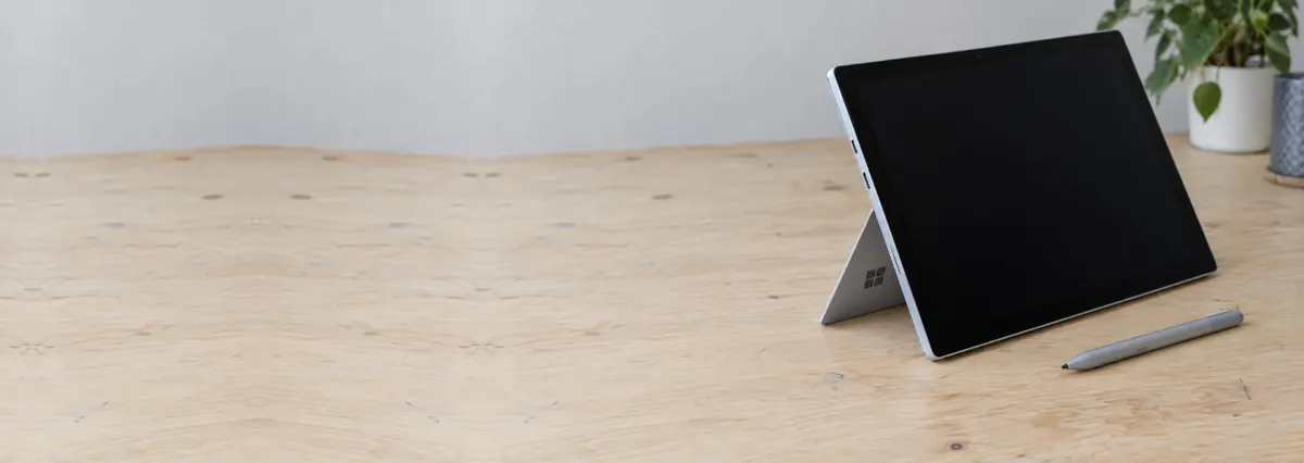 A Microsoft Surface Pro on its kickstand beside a stylus pen on a plywood bench