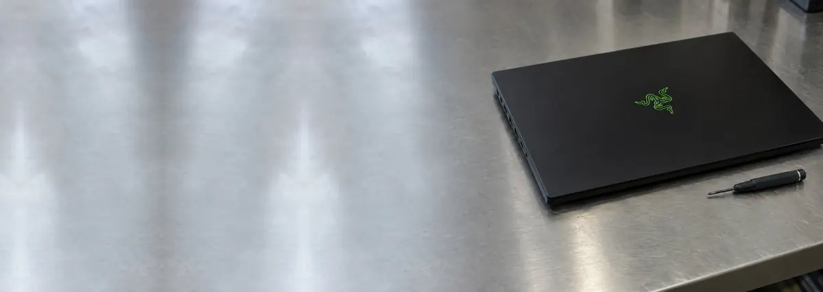 A closed black Razer Blade gaming laptop beside a screwdriver on a steel workbench