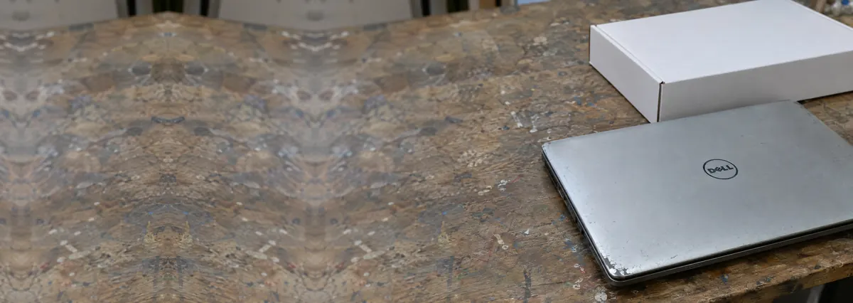 An older scuffed Dell laptop beside a plain white laptop box on a wooden bench