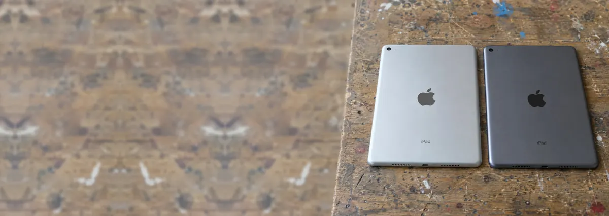 Two Apple iPads lying face-down on a wooden bench