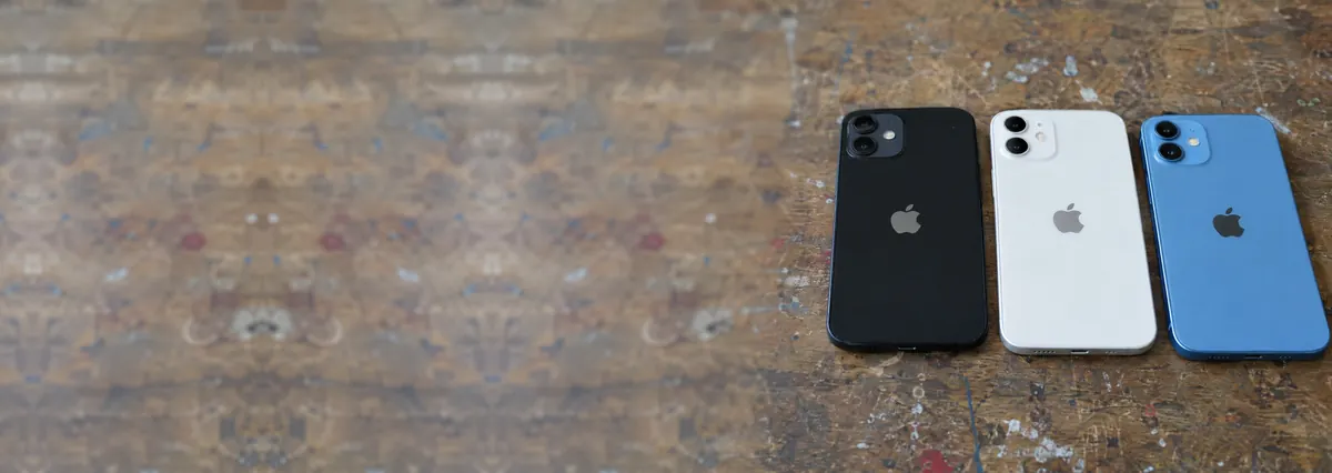 Three Apple iPhones lying face-down side by side on a wooden bench