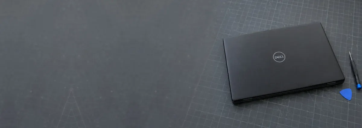 A closed black Dell laptop beside an opening pick and a screwdriver on a slate-grey workbench