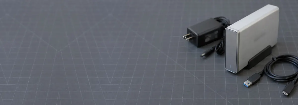 A desktop external hard drive with its power adapter and USB cable on a slate-grey workbench