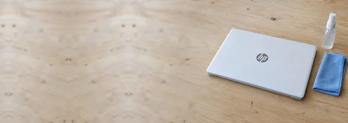 A closed white HP laptop beside a microfibre cloth and a spray bottle on a plywood bench