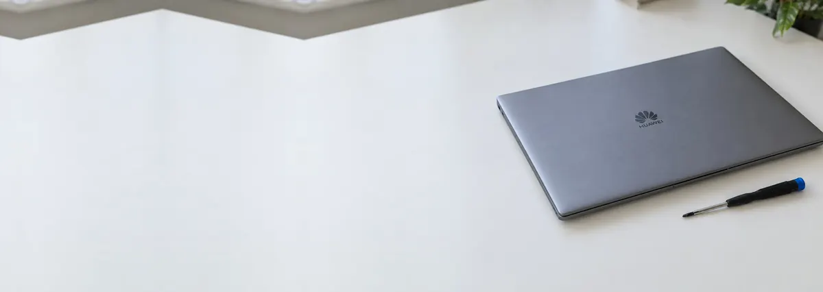 A closed space-grey Huawei laptop beside a screwdriver on a white bench