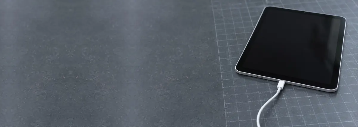 An Apple iPad with a USB-C cable plugged in on a slate-grey workbench