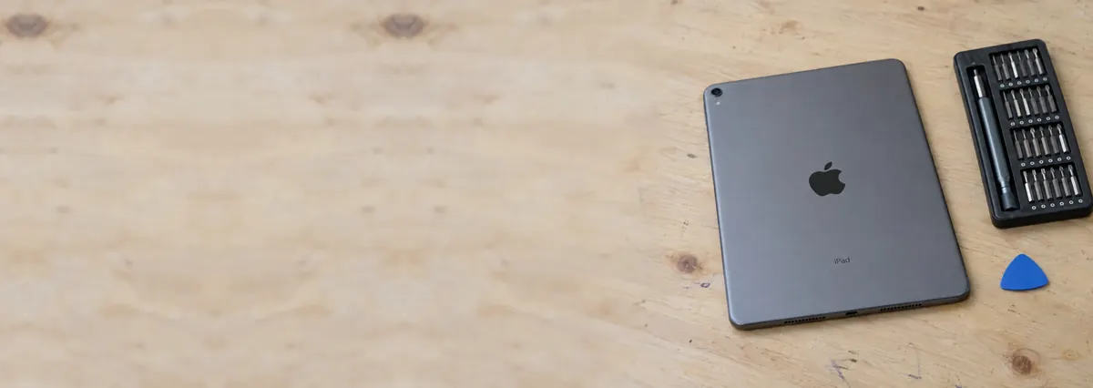 An Apple iPad lying face-down beside a screwdriver set and an opening pick on a plywood bench