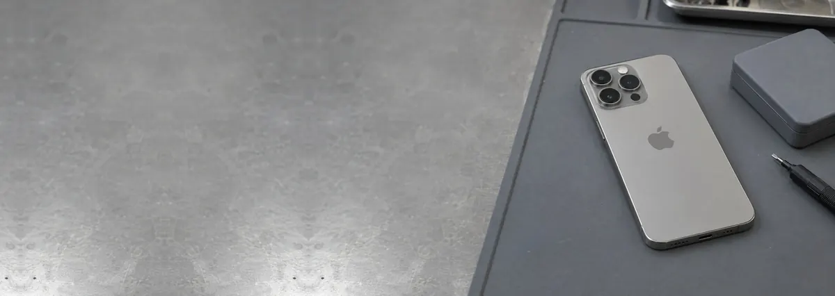 A natural-titanium Apple iPhone 15 Pro lying face-down on a grey anti-static mat
