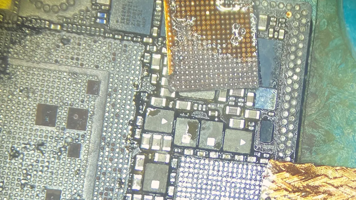 A phone logic board under the microscope, with a chip lifted and the solder pads beneath it