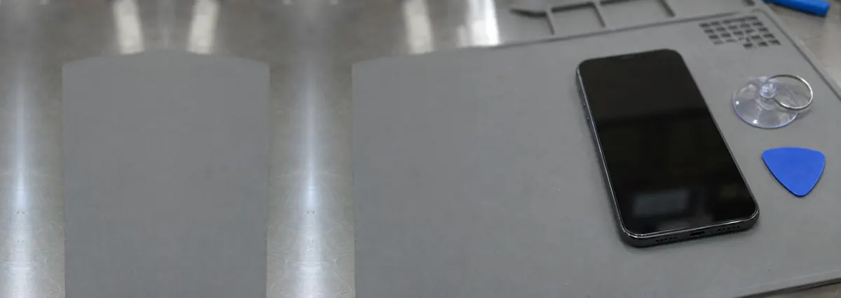 A smartphone lying face-up with its screen off beside a suction cup and an opening pick