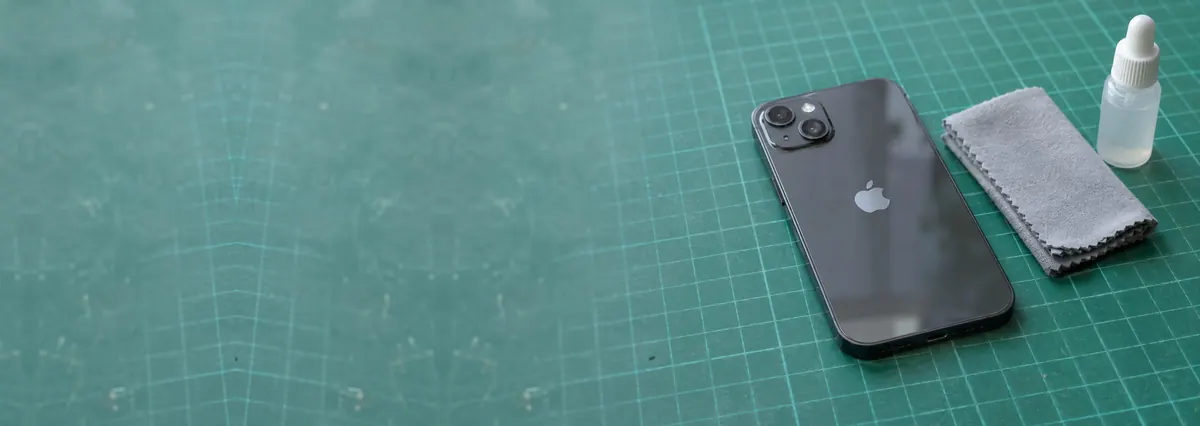 An Apple iPhone lying face-down beside a cloth and a dropper bottle on a green cutting mat