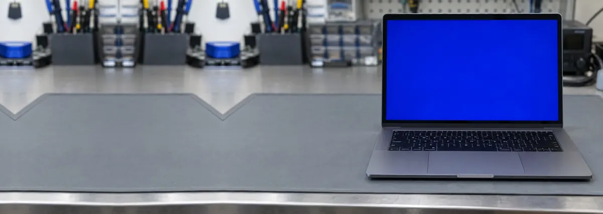An open laptop with a solid blue screen standing on a grey anti-static mat