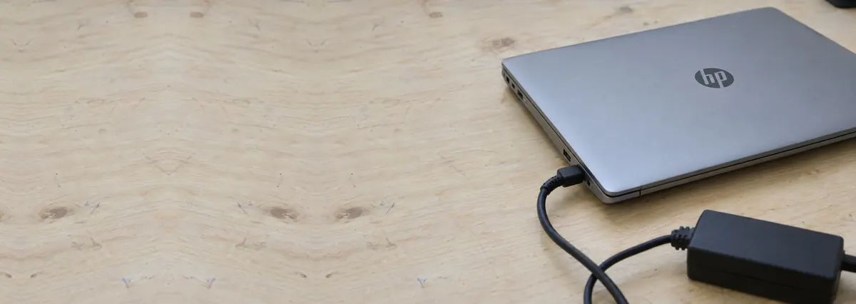 A closed HP laptop with a black charger plugged into its side on a plywood bench