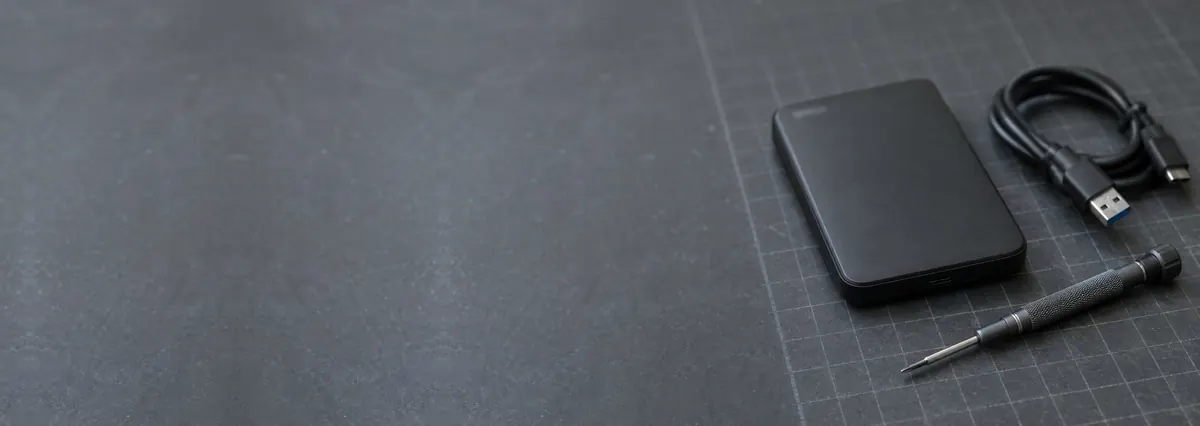 A black portable hard drive with a coiled USB cable on a slate-grey workbench