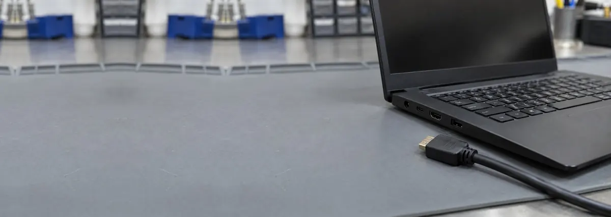 An open black laptop seen from the side showing its HDMI port, with an HDMI cable beside it