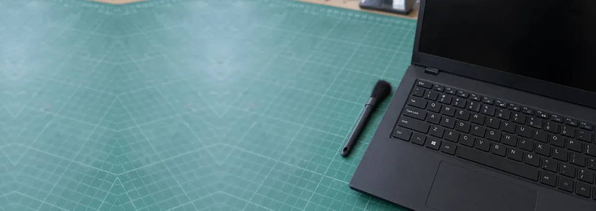 An open black laptop with its keyboard in focus beside a cleaning brush on a green cutting mat