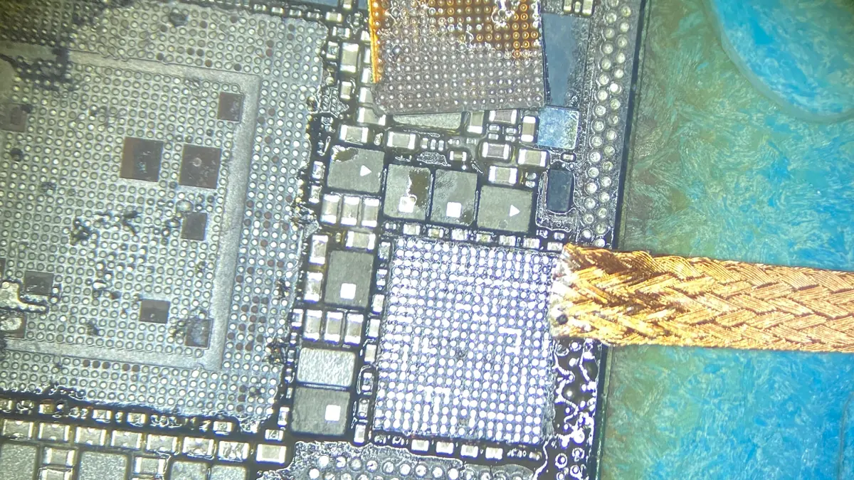 A circuit board under the microscope, with solder braid beside a lifted chip