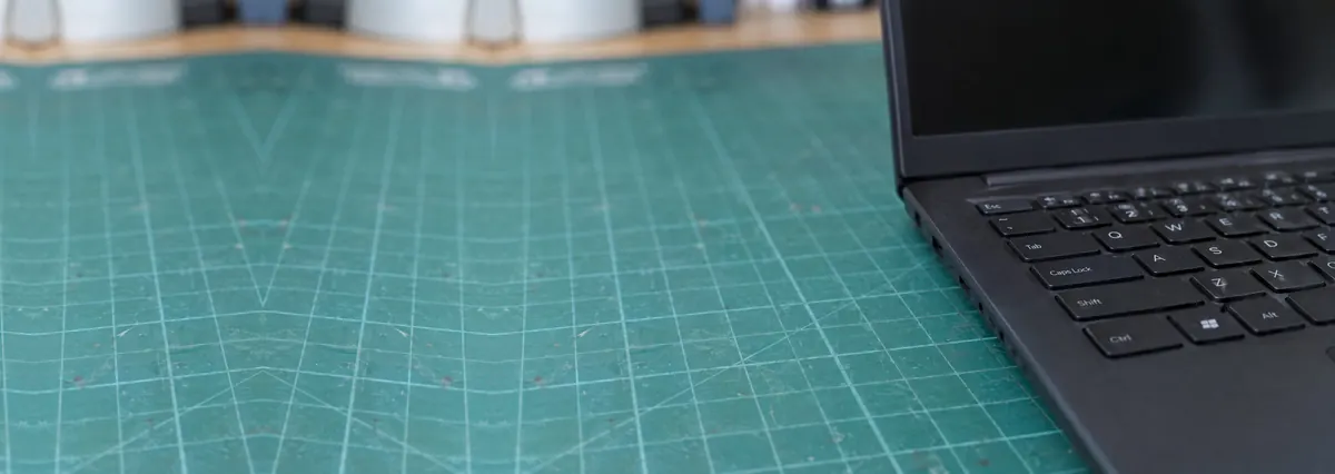 An open dark laptop seen from a low angle with its screen switched off on a green cutting mat