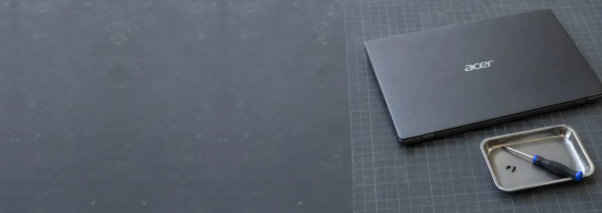 A closed Acer laptop beside a small screwdriver and a magnetic tray of screws on a slate-grey workbench