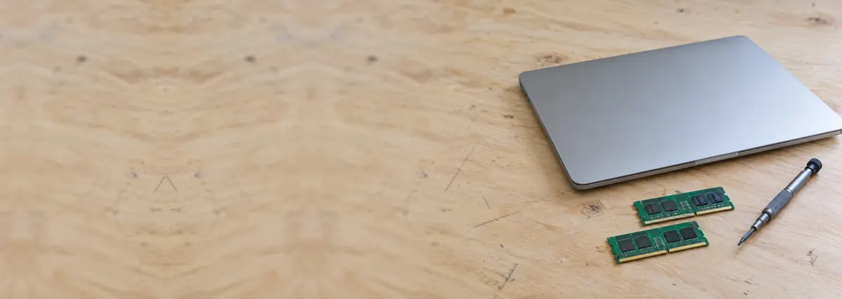 A closed laptop beside two memory modules and a screwdriver on a plywood bench
