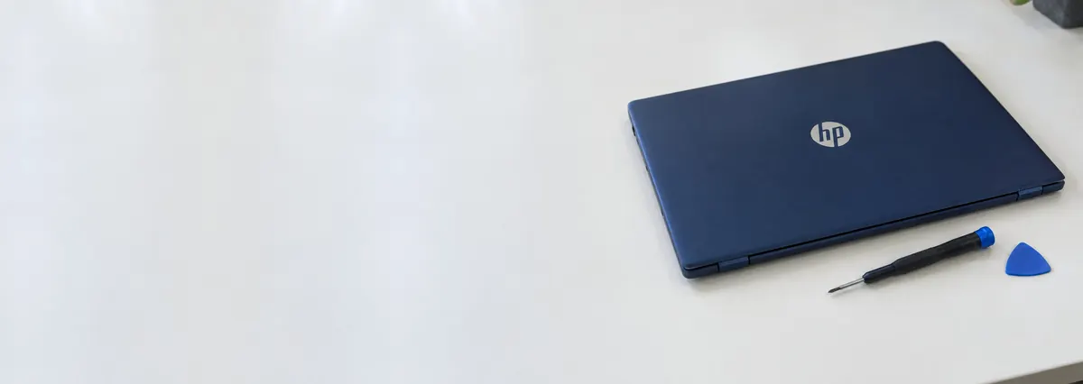 A closed navy-blue HP laptop beside a screwdriver and an opening pick on a white bench