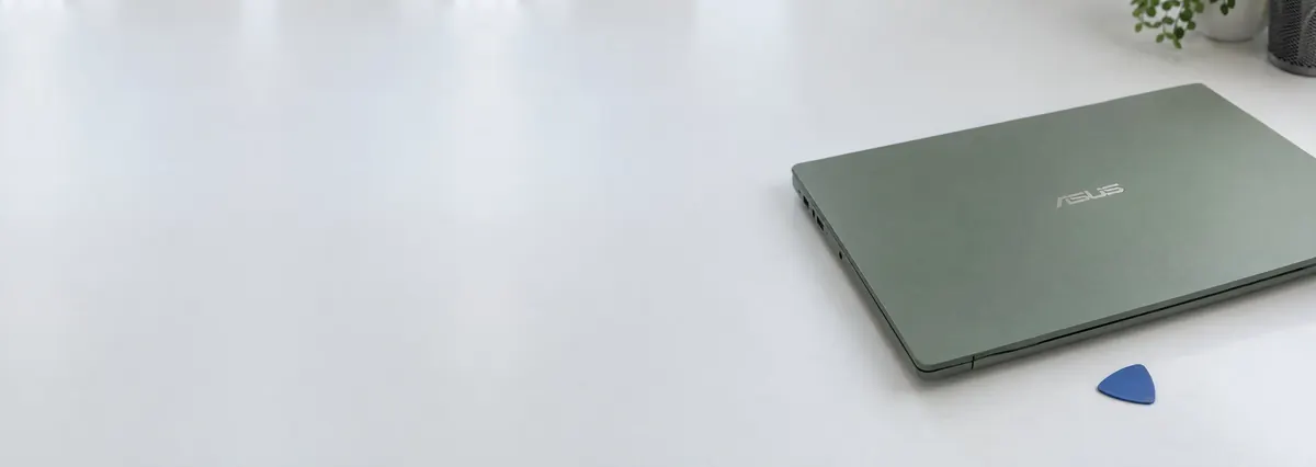 A closed sage-green ASUS laptop beside an opening pick on a white bench