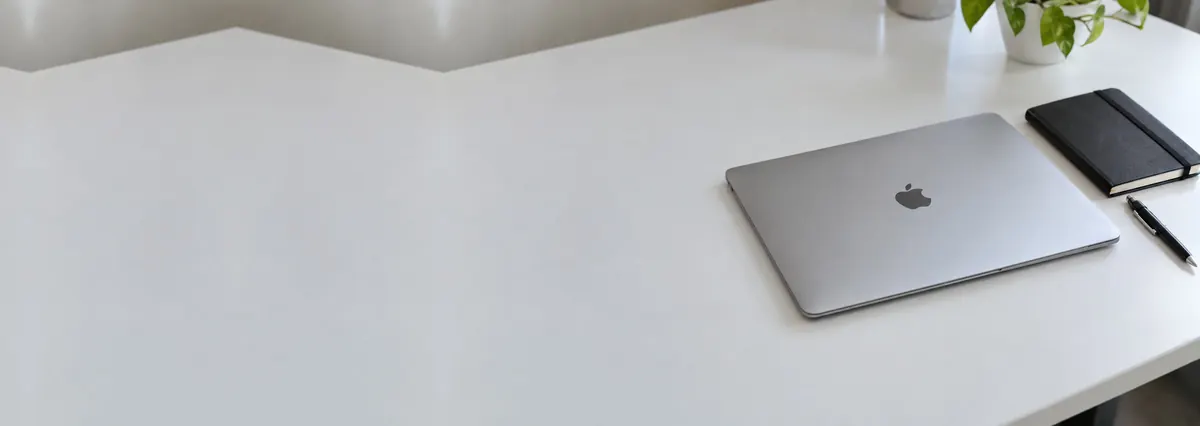 A slim silver Apple MacBook lying closed beside a small black notebook on a white bench