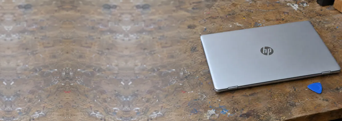 A closed silver HP laptop beside an opening pick on a wooden bench