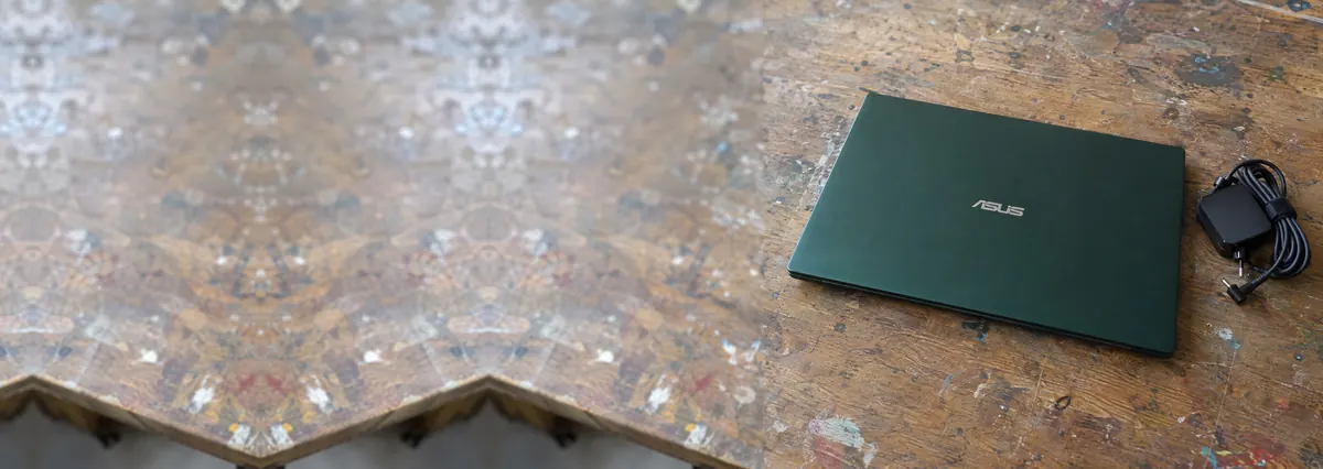 A closed dark-green ASUS laptop beside a coiled charger cable on a wooden repair bench