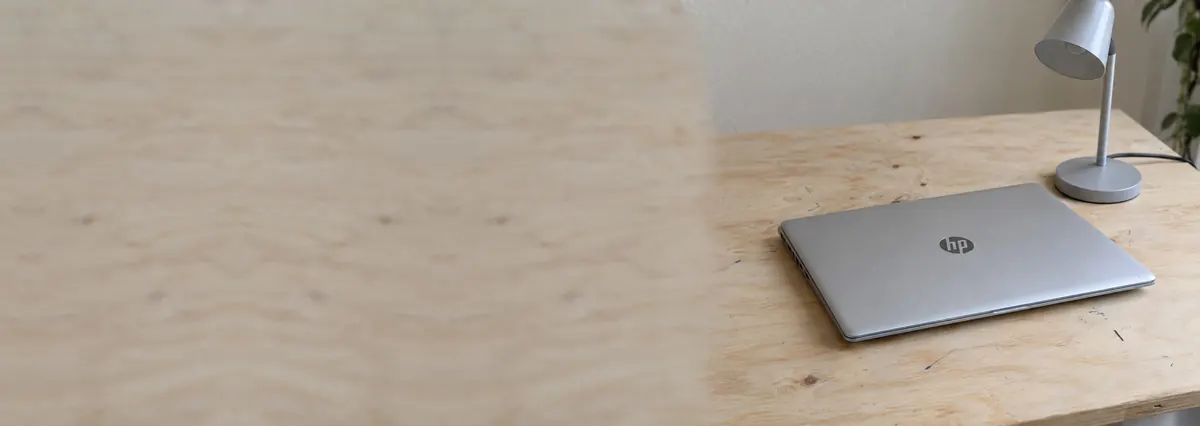A closed silver HP laptop beside a small desk lamp on a plywood bench