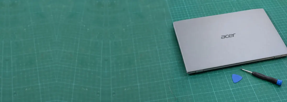 A closed light-grey Acer laptop beside an opening pick and a screwdriver on a green cutting mat