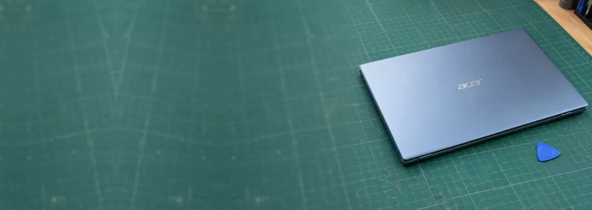 A closed silver-blue Acer laptop beside an opening pick on a green cutting mat